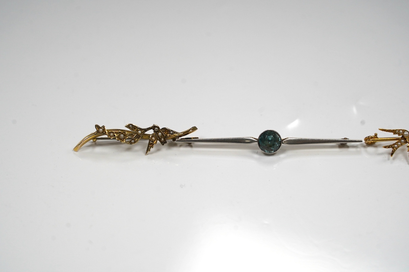 A 15ct and single stone blue zircon set bar brooch, 67mm and three other yellow metal and gem set bar brooches including seed pearl set swallow. Condition - fair